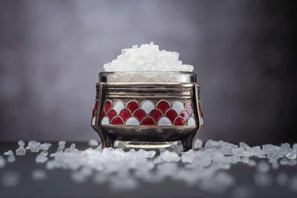 Close-up of crystal sea salt in a decorative jar with scattered salt on a dark background.