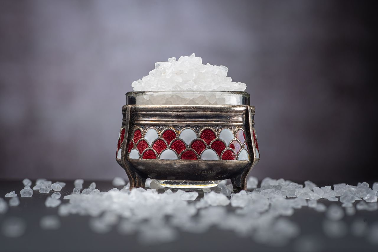 Boswellia Rivae: Ethiopian Frankincense (Mirafur), Composition, Origin and Uses Close-up of crystal sea salt in a decorative jar with scattered salt on a dark background.